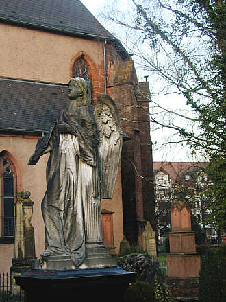 Engelsfigur auf dem alten Friedhof bei der Stiftskirche. Im Hintergrund der Chor der Kirche.