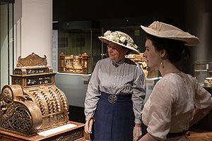 Zwei historisch gekleidete Damen vor einer Spielzeug-Kasse